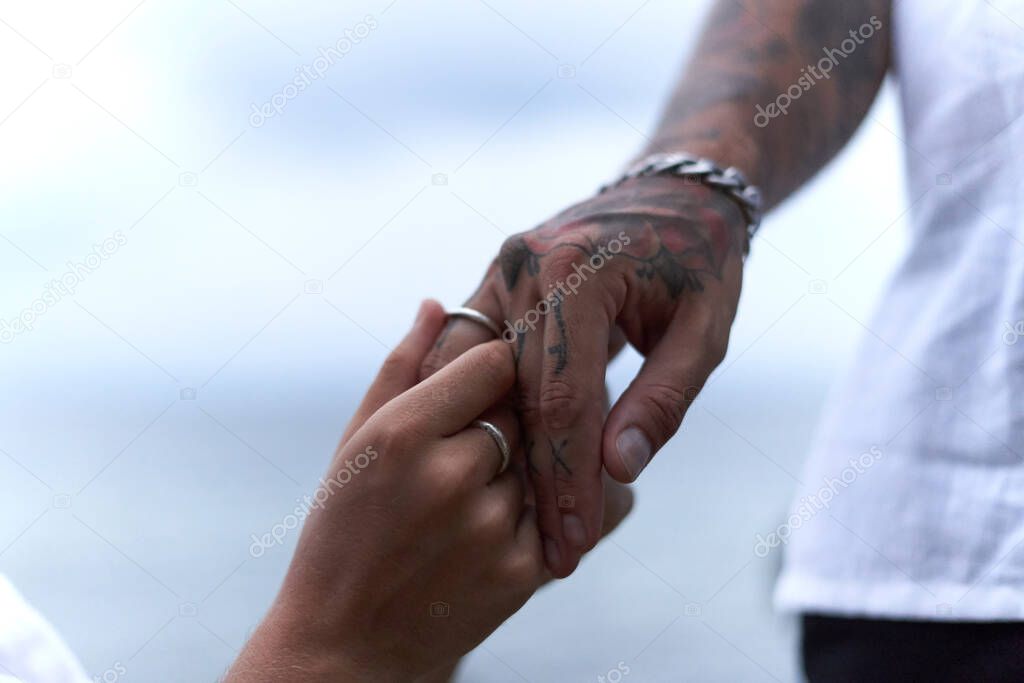 Male hand with a wedding ring while his gay partner holds his hand in marriage.