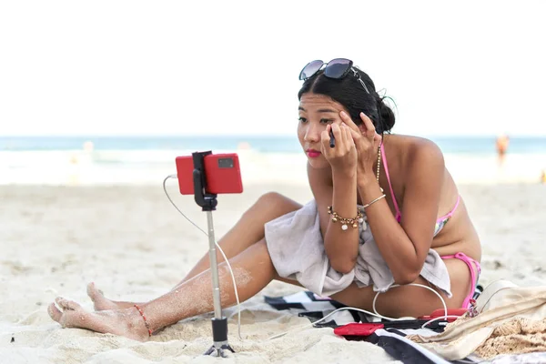 Asiatische junge Streamerin schminkt sich für eine Live-Übertragung vom Strand — Stockfoto