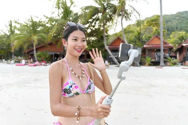 Sahilde selfie çubuğuna bağlanmış bir cep telefonunun kamerasına el sallayan bir flaş.