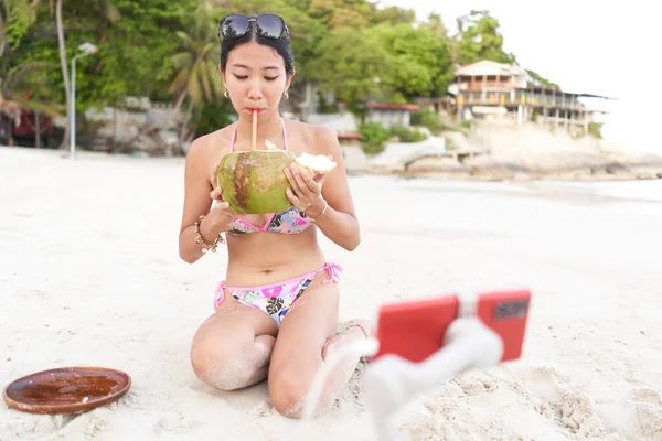 Sahilde cep telefonuyla yaşarken hindistan cevizi suyu içen bir flaş.