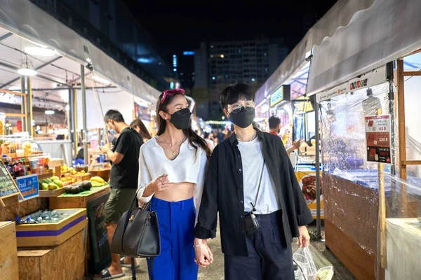 Pareja lesbiana en máscara caminando relajada a través de una feria nocturna urbana — Foto de Stock