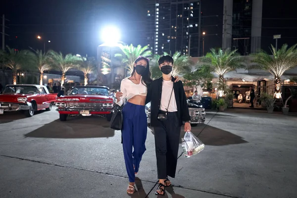 Lesbijki para z maską twarzy stoi na nocnym targu ulicznym z zabytkowymi samochodami — Zdjęcie stockowe
