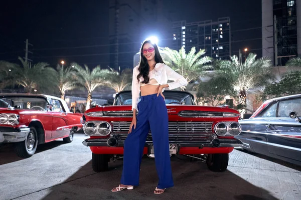 Schoonheid jonge vrouw poseren in de voorkant van een luxe antieke auto in een nacht kermis — Stockfoto
