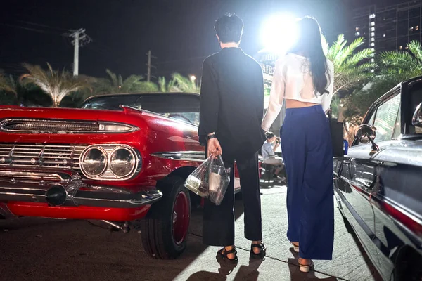 Lage hoek uitzicht van een lesbisch paar staan tussen vintage auto 's in een nacht beurs — Stockfoto