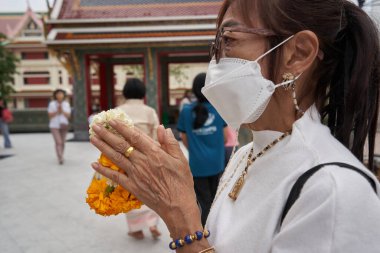 Bangkok, Tayland, 16 Şubat 2022: Makha Bucha Günü festivali sırasında Budist tapınağında dua eden yüz maskesi takan bir kadının profili