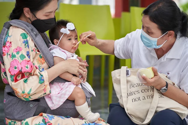 Bangkok, Tayland, 16 Şubat 2022: Yüzü maske takmış iki kadın sokakta bebek besliyor