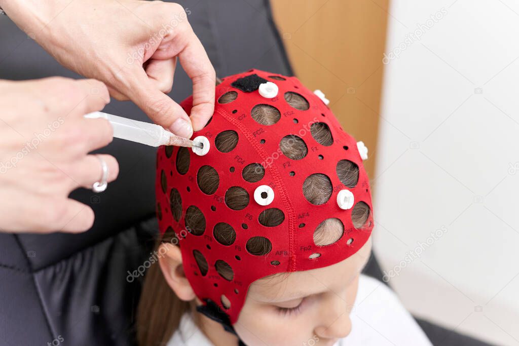 Top view of the hand of a doctor applying a liquid to a patients headgear for biofeedback therapy.