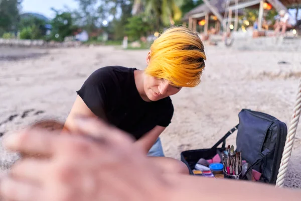 Focus on an artist painting a woman during a body paint session on the beach