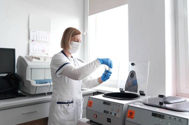 Doktor, bir hastanede santrifüjün reaksiyon kabını kullanırken elinde numuneyle bir tüp tutuyor.