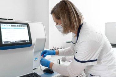 Koruyucu teçhizatlı teknisyen hastane laboratuvarında reaksiyon aracıyla çalışıyor.