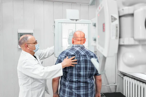 Doctor correctly positioning a patient in front of an x-ray machine in an hospital room