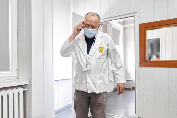 Betagter Arzt Mit Maske Gespräch Mit Einem Handy Krankenhaus Stockfoto