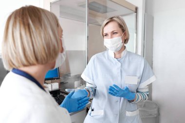 Yüz maskeli iki doktor hastanede konuşuyor.