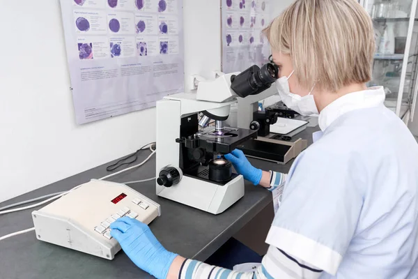 Technician of a laboratory sitting on a desk while using a microscope in a lab of an hospital