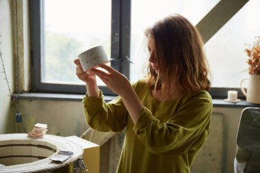 Kil ürünü inceleyen heyecanlı seramistin portresi. Çömlek atölyesinde çalışan kadın seramik. Çömlek yapma süreci. Usta seramist onun stüdyosunda çalışıyor.