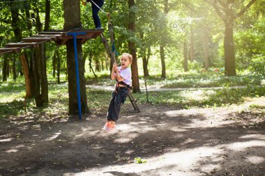 Macera halat parkında ip köprüde yürüyen cesur küçük bir kızın portresi. Macera parkında eğleniyorum. İp atma alıştırması yapan izci.