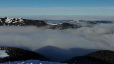 Drone kış dağlarında sis denizinin üzerinde uçar. Karda güneşli bir gün Karpatlar 'ı kapladı. Gökyüzündeki bulutlar