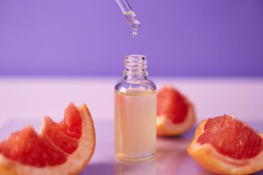 Citrus ya da greyfurt esaslı yağı cam şişede moda mor arka planda taze greyfurtla birlikte. Spa ve cilt ürünleri