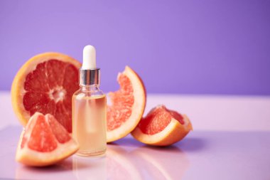 Citrus ya da greyfurt esaslı yağı cam şişede moda mor arka planda taze greyfurtla birlikte. Spa ve cilt ürünleri