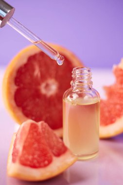 Citrus ya da greyfurt esaslı yağı cam şişede moda mor arka planda taze greyfurtla birlikte. Spa ve cilt ürünleri