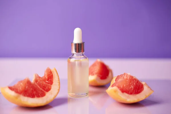 玻璃瓶中的柑橘类或柚子精油 带有新鲜柚子 背景呈紫色 温泉及护肤产品 — 图库照片