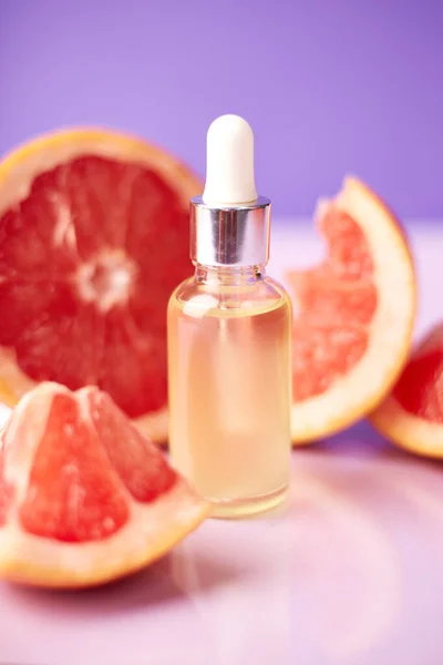 Citrus ya da greyfurt esaslı yağı cam şişede moda mor arka planda taze greyfurtla birlikte. Spa ve cilt ürünleri