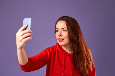 Mor arka planda cep telefonunu kullanan kırmızı elbiseli beyaz kadının yakın portresi.