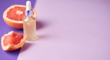 Citrus ya da greyfurt esaslı yağı cam şişede moda mor arka planda taze greyfurtla birlikte. Spa ve cilt ürünleri