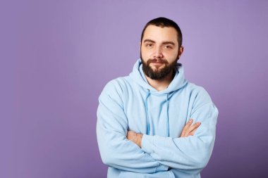 Mutlu sakallı adam mor arka planda mavi kazak giyer. Dostça gülümseme. Boşluğu kopyala