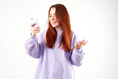 Mor kazaklı beyaz bir kadın. Doğal görünüş. Gülümsüyor. Uzun kızıl saçlı. Beyaz arkaplan