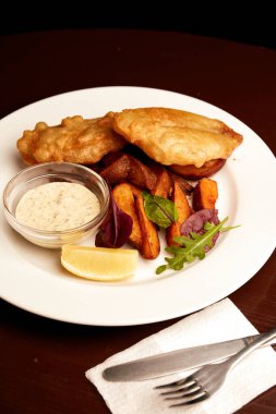 Bir tabakta haşlanmış balık ve pubda tahta bir masada patates kızartması. Sağlıksız yiyecekler