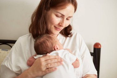 Anne yeni doğmuş bebeğini kucağında tutuyor. Yeni doğan anne ve bebeğin ev portresi. Birlikte eğleniyoruz.