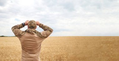 Buğday tarlasında Ukraynalı bir asker. Ukrayna buğday tarlaları ve yaklaşan gıda krizi. Ukrayna Silahlı Kuvvetleri