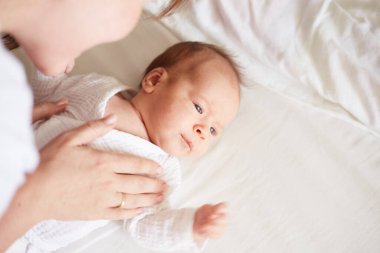 Mother dress her newborn baby boy. Realistic home portrait