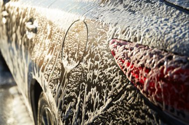 Family cleaning car in self-service at car wash during sunset. Car covered in white foam. Concept of easy and fun self-service