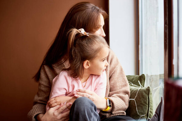 Little caucasian girl with mother looking at window and dreaming. A lot of gift boxes around. Happy family christmas concept