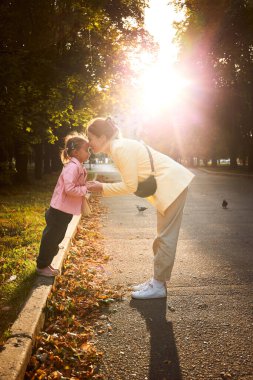 Anne ve kızının günbatımında sonbahar parkında çekilmiş otantik bir portresi. Birlikte eğleniyoruz.