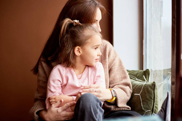 Little caucasian girl with mother looking at window and dreaming. A lot of gift boxes around. Happy family christmas concept