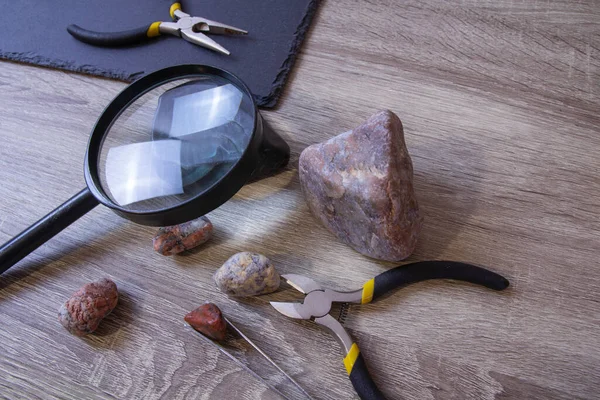 Stones, black rocks lie on the table with two forceps and a magnifying glass — Stockfoto
