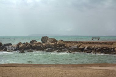Akdeniz manzarası. Kıyı taşları, bulutlu gökyüzü, deniz manzarası. Dükkan uzaktaki iskelede duruyor. İspanya, Alicante, Costa Blanca