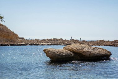 A beautiful view of the sea bay with large stones in the foreground, fishermen in the background. View from afar. Campello, Spain.