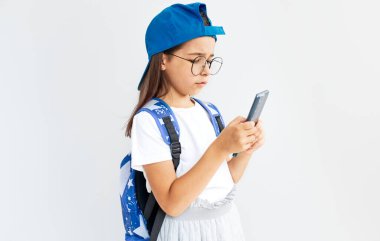 Mavi şapkalı, beyaz tişörtlü, şeffaf gözlüklü ve beyaz arka planda akıllı telefon taşıyan sevimli bir çocuk. Cep telefonuyla online oyun oynayan küçük bir kız. Çocuk internetten öğreniyor.