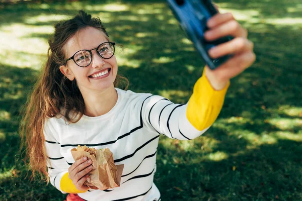 캠퍼스의 풀밭에서 식사중 셀카를 미소짓는 여학생 친구에게 사진을 보내고 스마트폰으로 로열티 프리 스톡 이미지