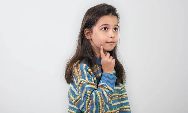 明るい灰色のスタジオの背景の上にポーズを取る片側を見てカラフルなセーターを着ている小さな子供 思いやりのある少女が何かを考えて — ストック写真
