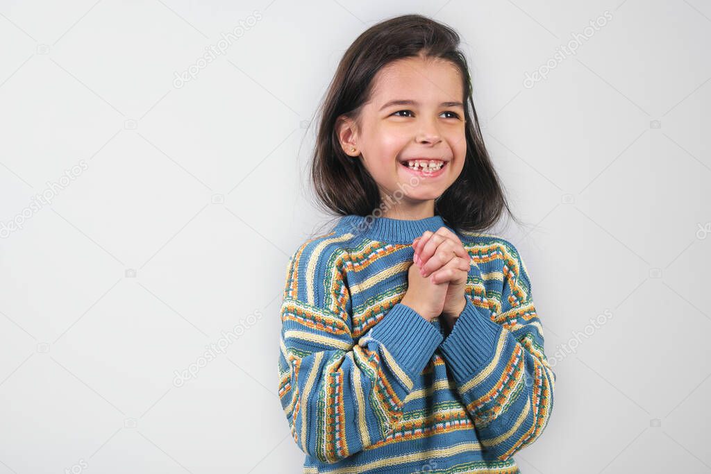 Happy Caucasian cute little girl wearing a colorful sweater and smiling broadly isolated on grey background. A pretty child has positive and joyful emotions during waiting for Christmas presents.