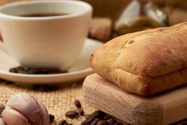 Etrafına Amerikan usulü kahve, zeytinyağı, kahve çekirdeği ve sarımsak konmuş sebze lifinin içine konmuş bir kase kırsal ekmek.