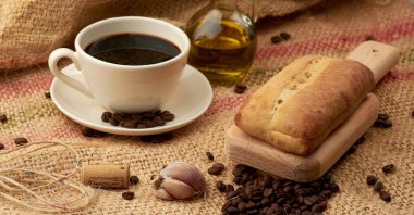 Etrafına Amerikan usulü kahve, zeytinyağı, kahve çekirdeği ve sarımsak konmuş sebze lifinin içine konmuş bir kase kırsal ekmek.