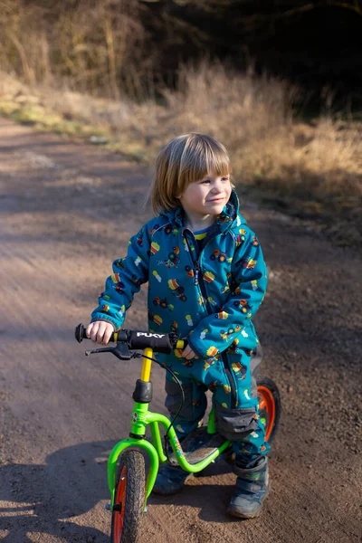 Szczęśliwy 3 lat stary chłopiec w niebieski ogólny jazda na zielony rower równowagi — Zdjęcie stockowe