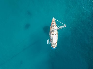 Akdeniz 'de turkuaz safirli sularla dolu tropikal plaja yanaşmış bir teknenin kuş bakışı dronu.