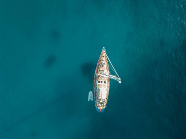 Akdeniz 'de turkuaz safirli sularla dolu tropikal plaja yanaşmış bir teknenin kuş bakışı dronu.
